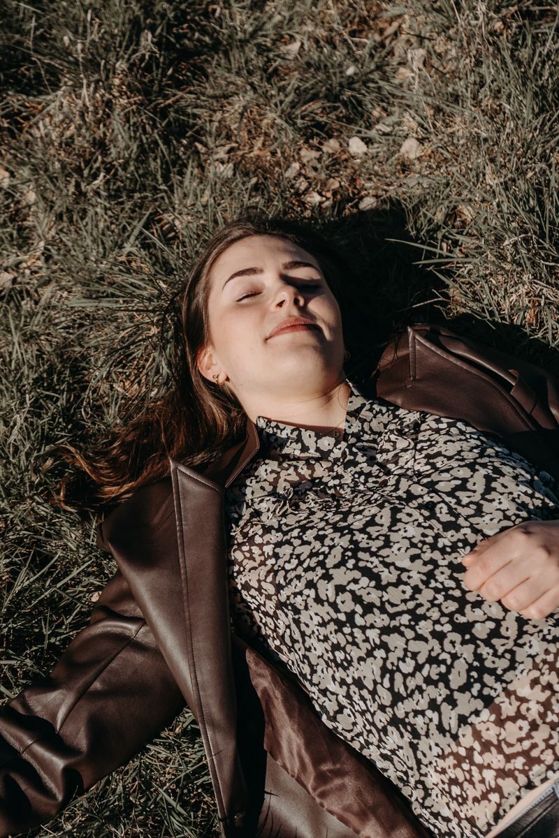 Portrait of a woman lying on grass with eyes closed, enjoying the sun outdoors.