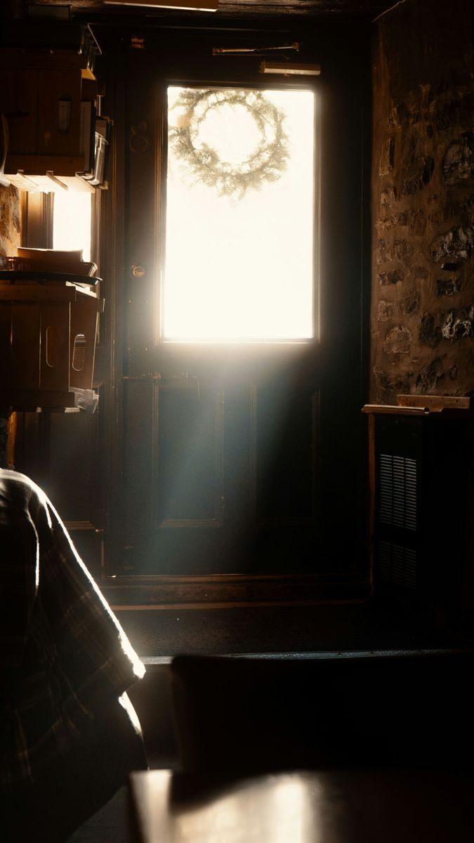 Warm sunlight streaming through a door with wreath in a rustic room.