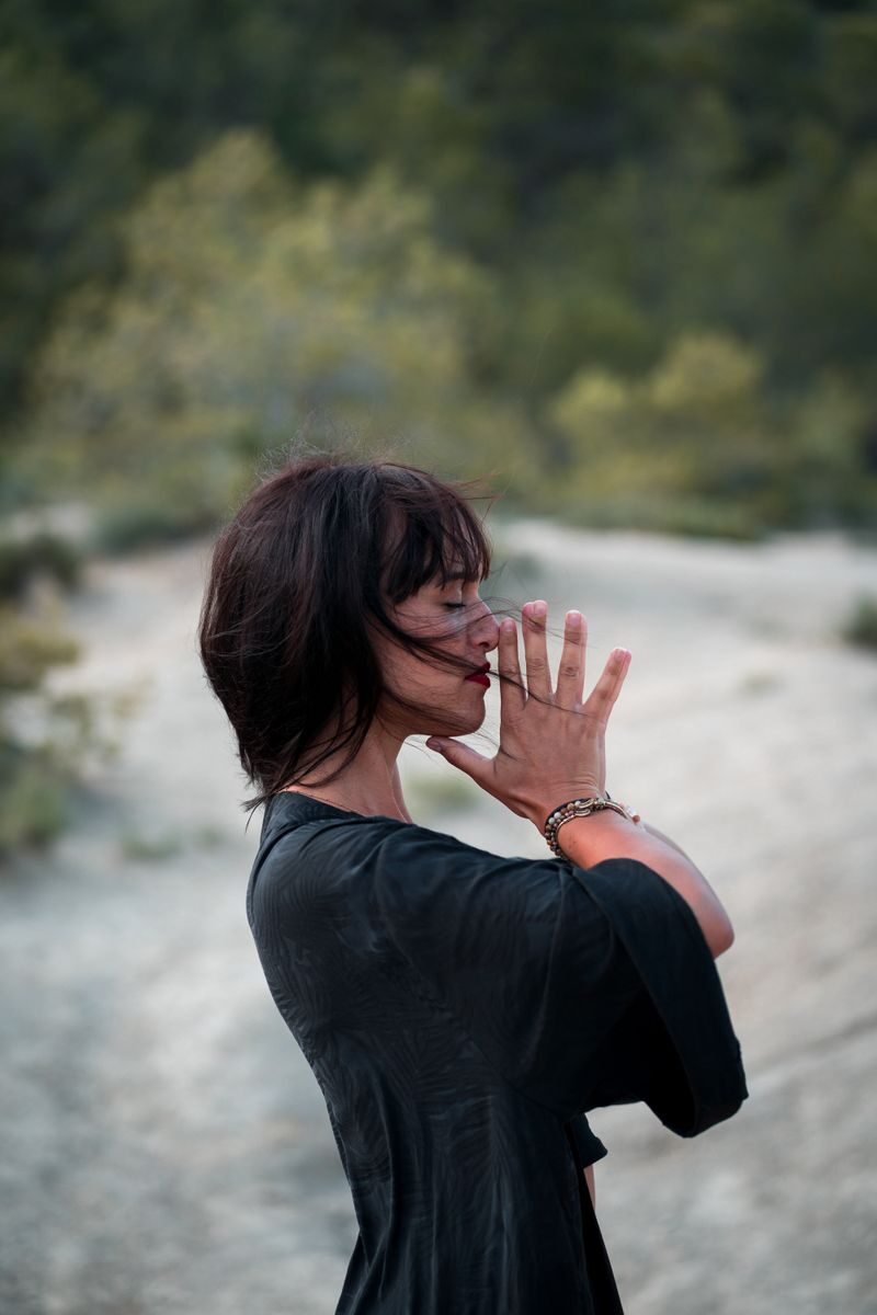Side view of calm woman with closed eyes praying in windy weather against green trees